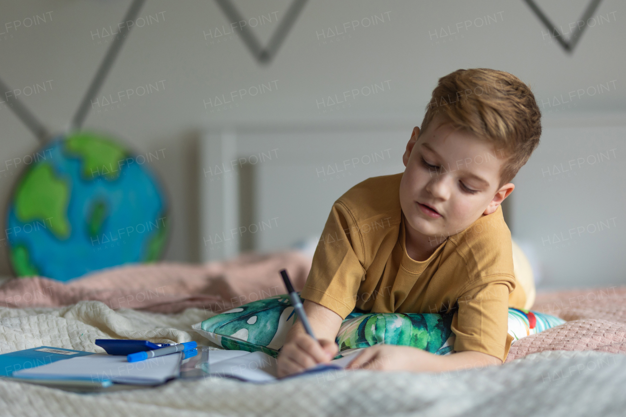 Little boy lying on a bed and doing the homework.