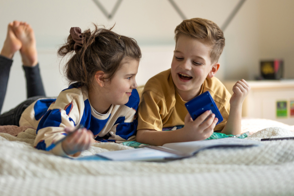 Little children lying on bed and doing their homework.