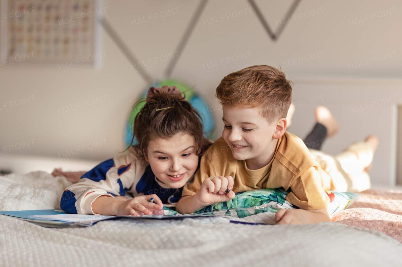 Little children lying on bed and doing their homework.