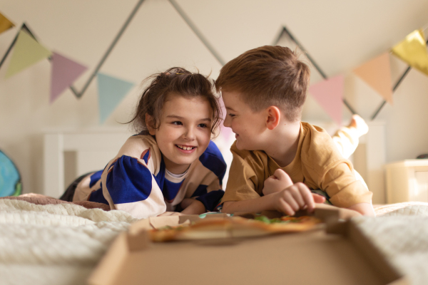 Happy friends lying on a bed and eating a pizza.