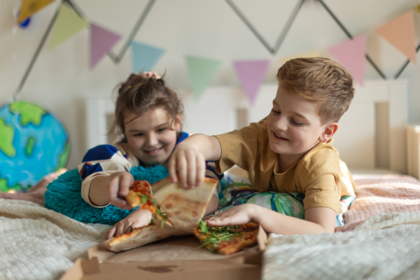 Happy friends lying on a bed and eating a pizza.