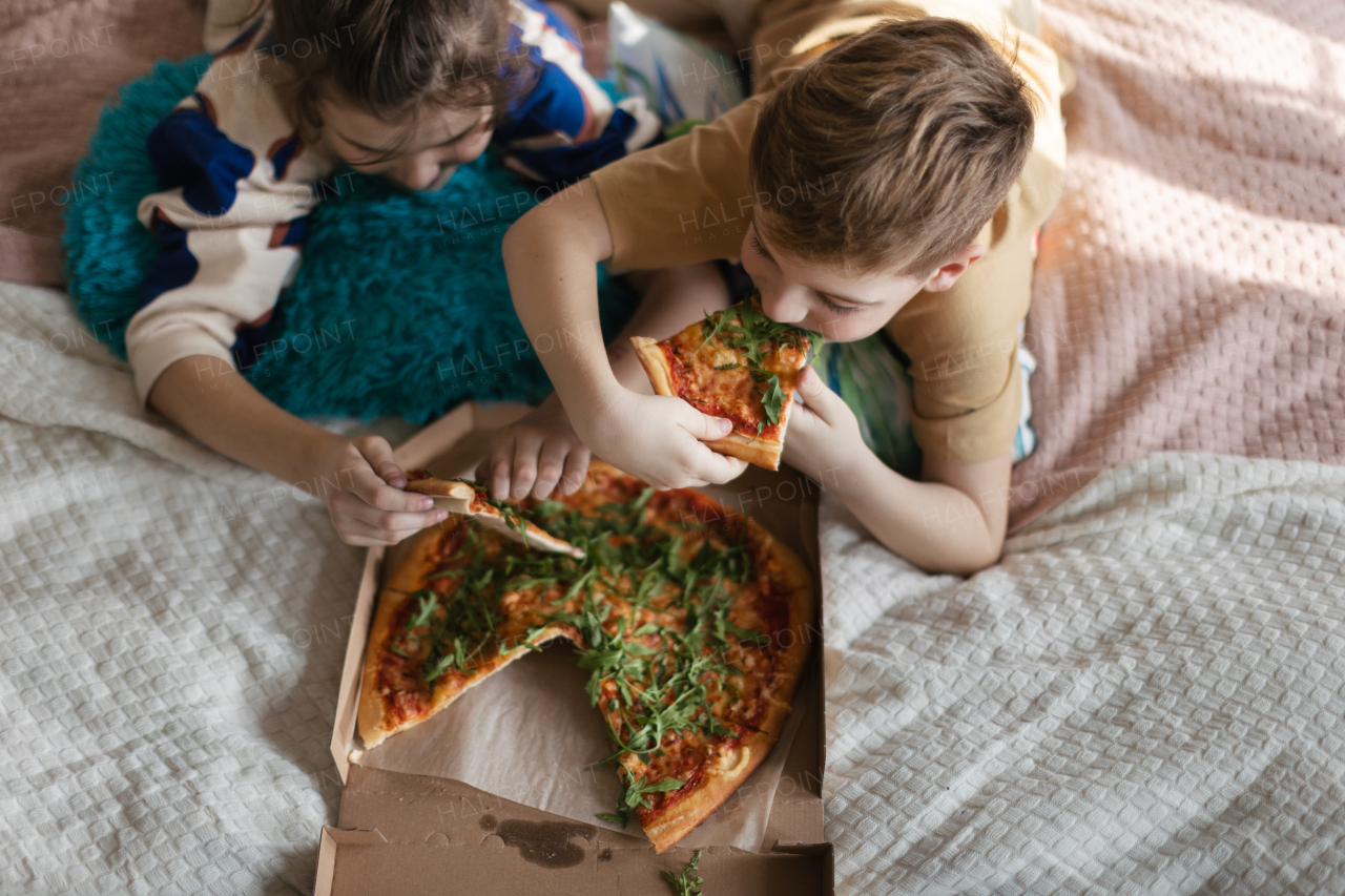 Top view of friends lying on a bed and eating a pizza. Eating food in the bedroom.