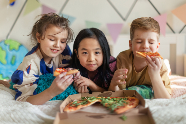 Happy friends lying on a bed and eating a pizza.