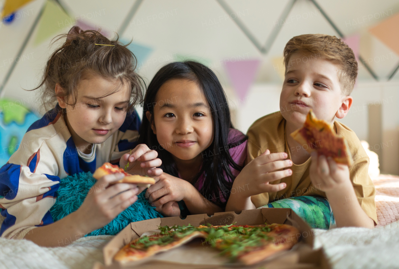 Happy friends lying on a bed and eating a pizza.