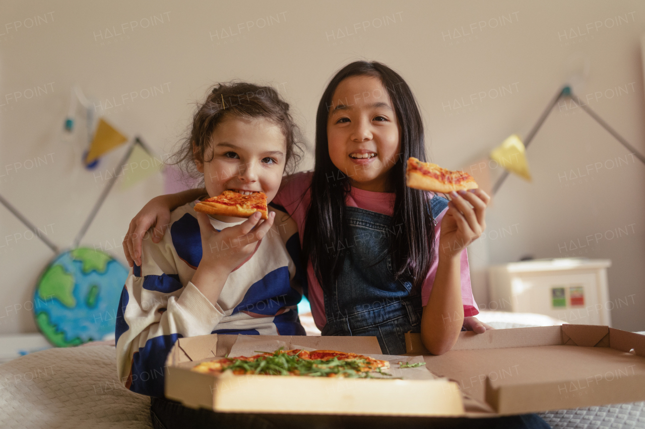 Happy friends lying on a bed and eating a pizza.