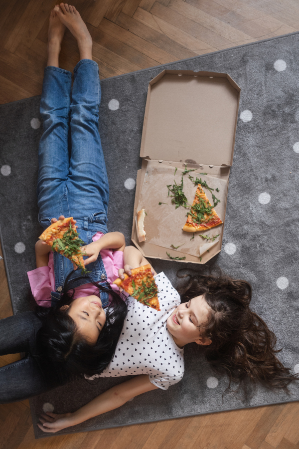 Happy friends lying on a floor and eating a pizza.