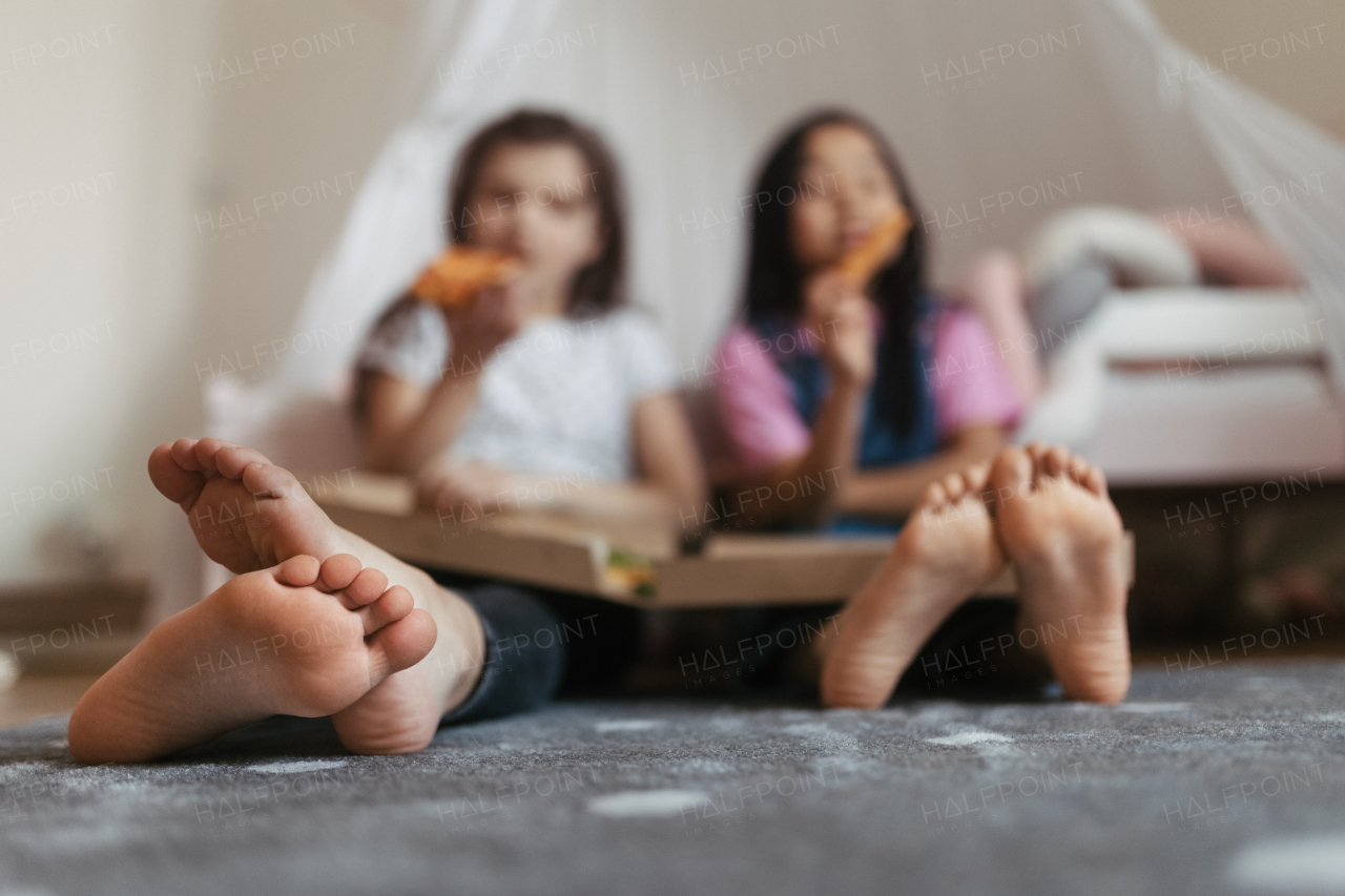 Friends sit on the floor with pizza box in their lap. Eating food in the bedroom.