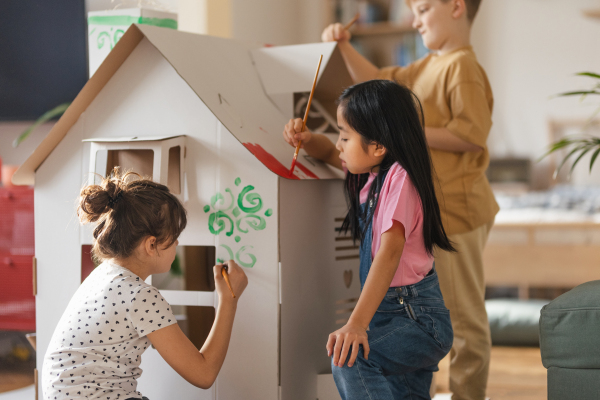 Happy children painting handmade carboard house together, having fun.