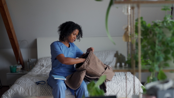 Female nurse or doctor in scrubs unpacking backpack in bedroom, after long work day. Work-life balance for healthcare worker.