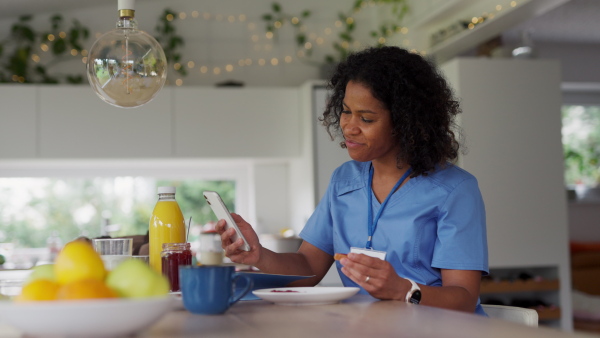 Female nurse or doctor getting ready for work in the morning, eating breakfast and having cup of coffee, before leaving for the work dressed in scrubs. Work-life balance for healthcare worker.