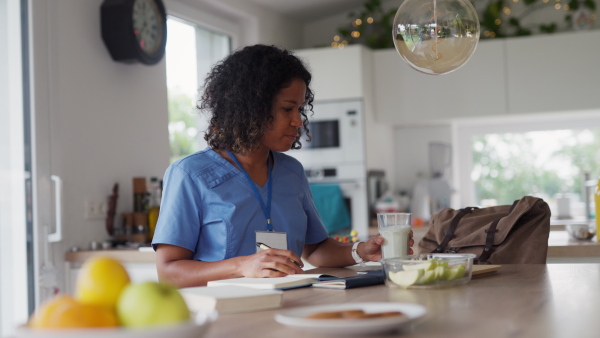 Female nurse or doctor getting ready for work in the morning, making to-do list, having breakfast, drinking glass of milk, before leaving for the work. Work-life balance for healthcare worker.