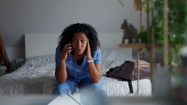 Female doctor dealing with work issues from home, after workday. Doctor making phone call on smartphone, telemedicine consultation, telehealth. Work-life balance for healthcare worker.