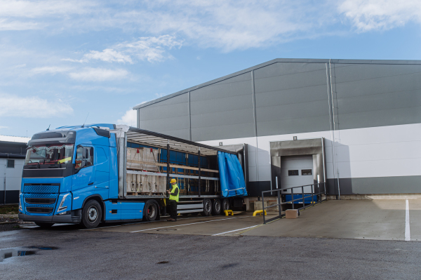 Warehouse receiver, worker standing by blue truck, holding tablet, looking at cargo details, checking delivered items or goods against order.