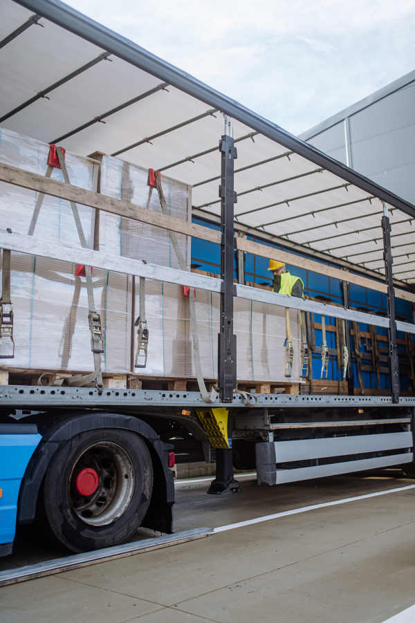 Side view of warehouse receiver standing inside of truck in cargo area, open trailer. Receiving clerk holding tablet, looking at cargo details, checking delivered items, goods against order.