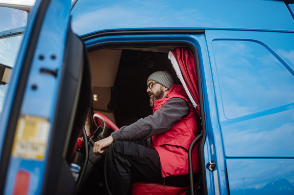 Portrait of confident professional truck driver sitting in a truck cabin, looking at camera and smiling.