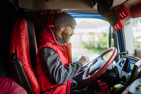 Truck driver sitting in truck, holding tablet, looking at cargo details, delivery schedule. Concept of load management.