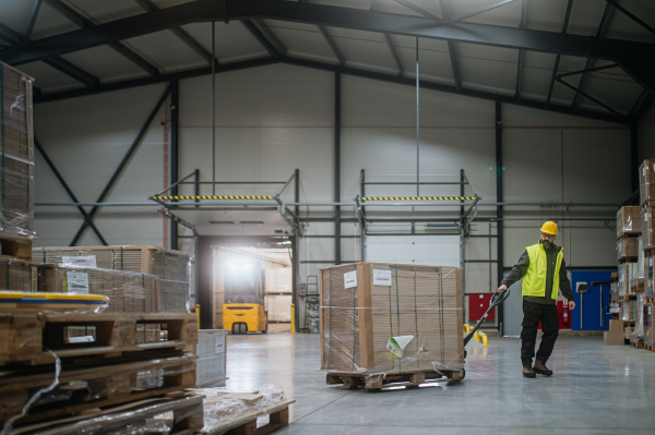 Warehouse worker maneuvering a pallet jack loaded with goods through the warehouse.