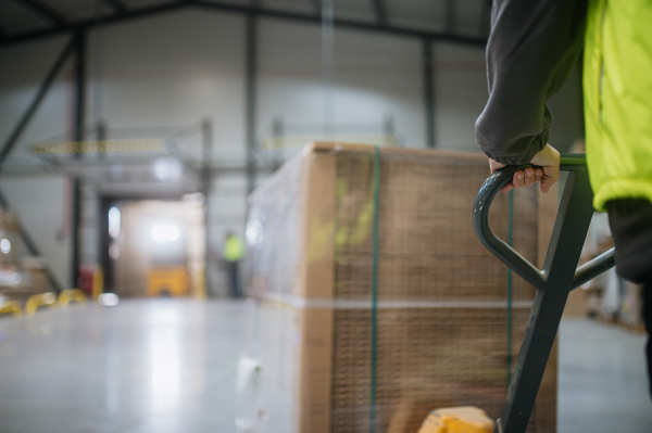 Close up of warehouse worker maneuvering a pallet jack loaded with goods through the warehouse.