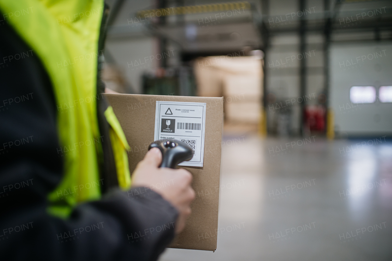 Warehouse worker scanning barcode on the cardboard box. Receiving clerk holding scanner checking delivered goods against order.