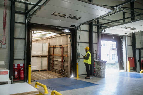 Warehouse receiver, clark overseeing the storing of delivered items, holding tablet, looking at cargo details.