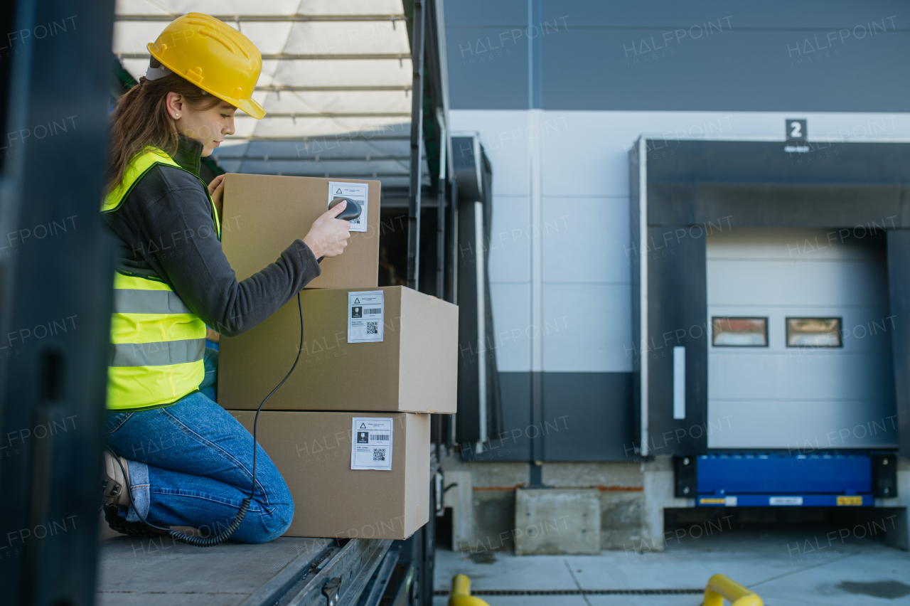 Female warehouse receiver kneeling inside of truck in cargo area, trailer, barcode scanning delivered items. Receiving clerk holding scanner checking delivered goods against order.