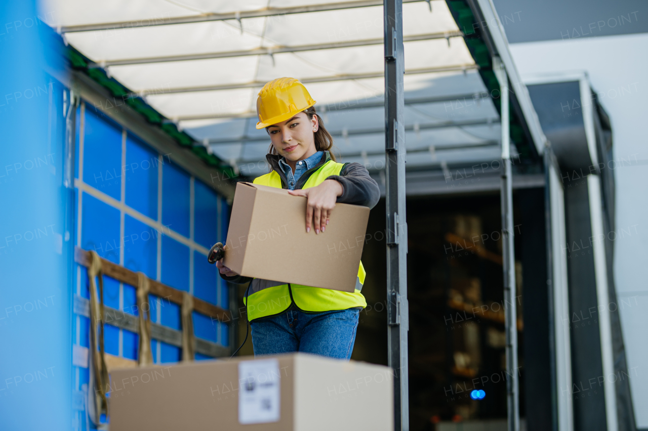 Female warehouse receiver standing inside of truck in cargo area, trailer, barcode scanning delivered items. Receiving clerk holding scanner checking delivered goods against order.