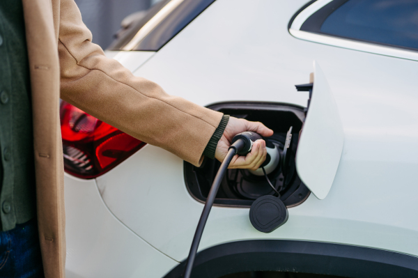 Close up of businessman charging electric car before going to office. An electric vehicle charging station in front of the office building. Charging at work, workplace.