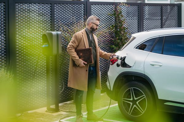 Businessman charging electric car before going to office. An electric vehicle charging station in front of the office building. Charging at work, workplace.