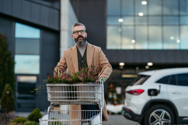 Man charging his electric car before going to shopping. A public charging station in front of shop building, supermarket. Charging while shopping.