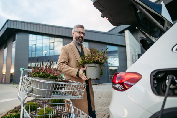 Man charging his electric car before going to shopping. A public charging station in front of shop building, supermarket. Charging while shopping.