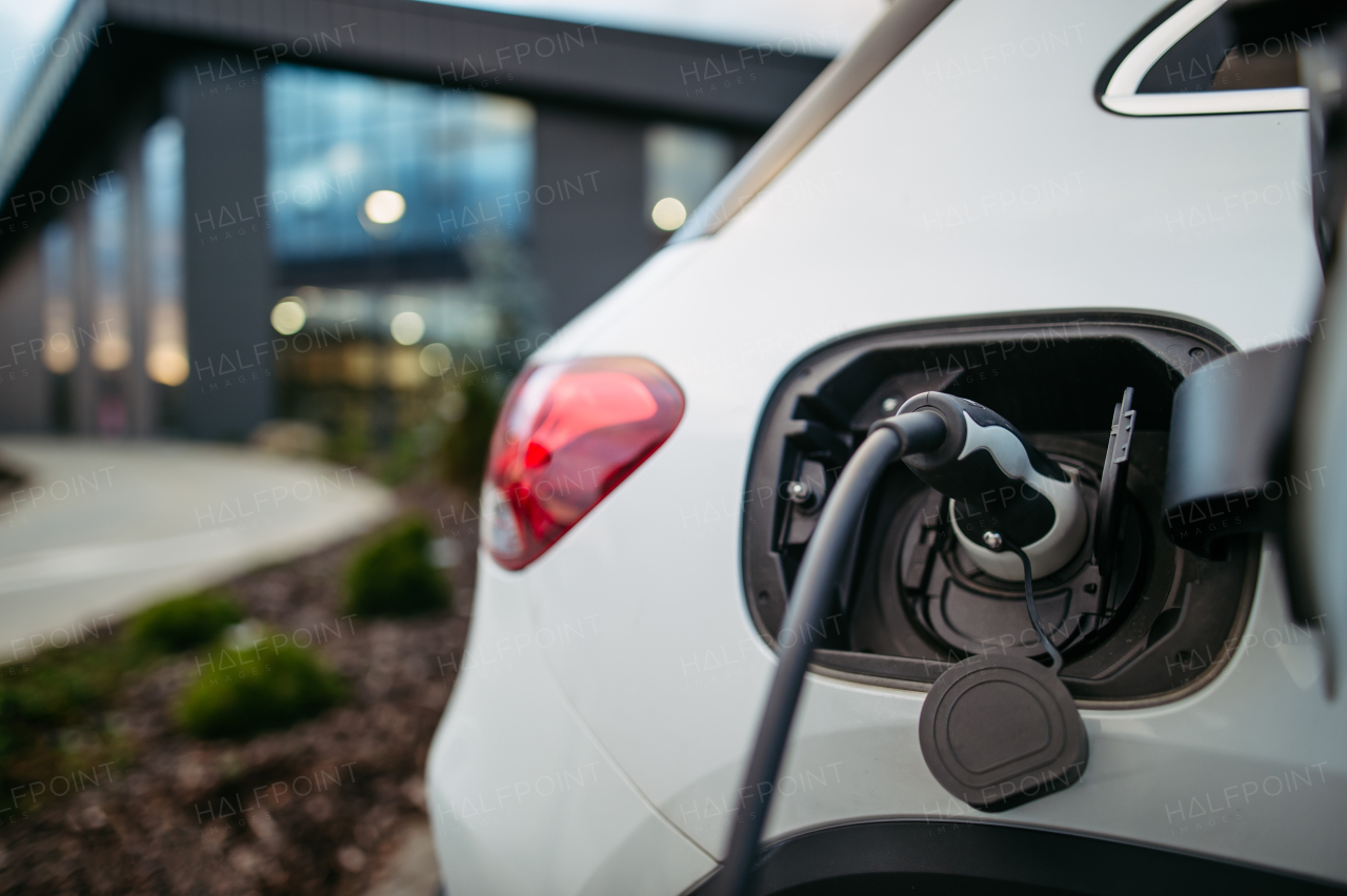 Close up electric car charging in front of office building. Vehicle with charging cable. Charging at work, workplace.