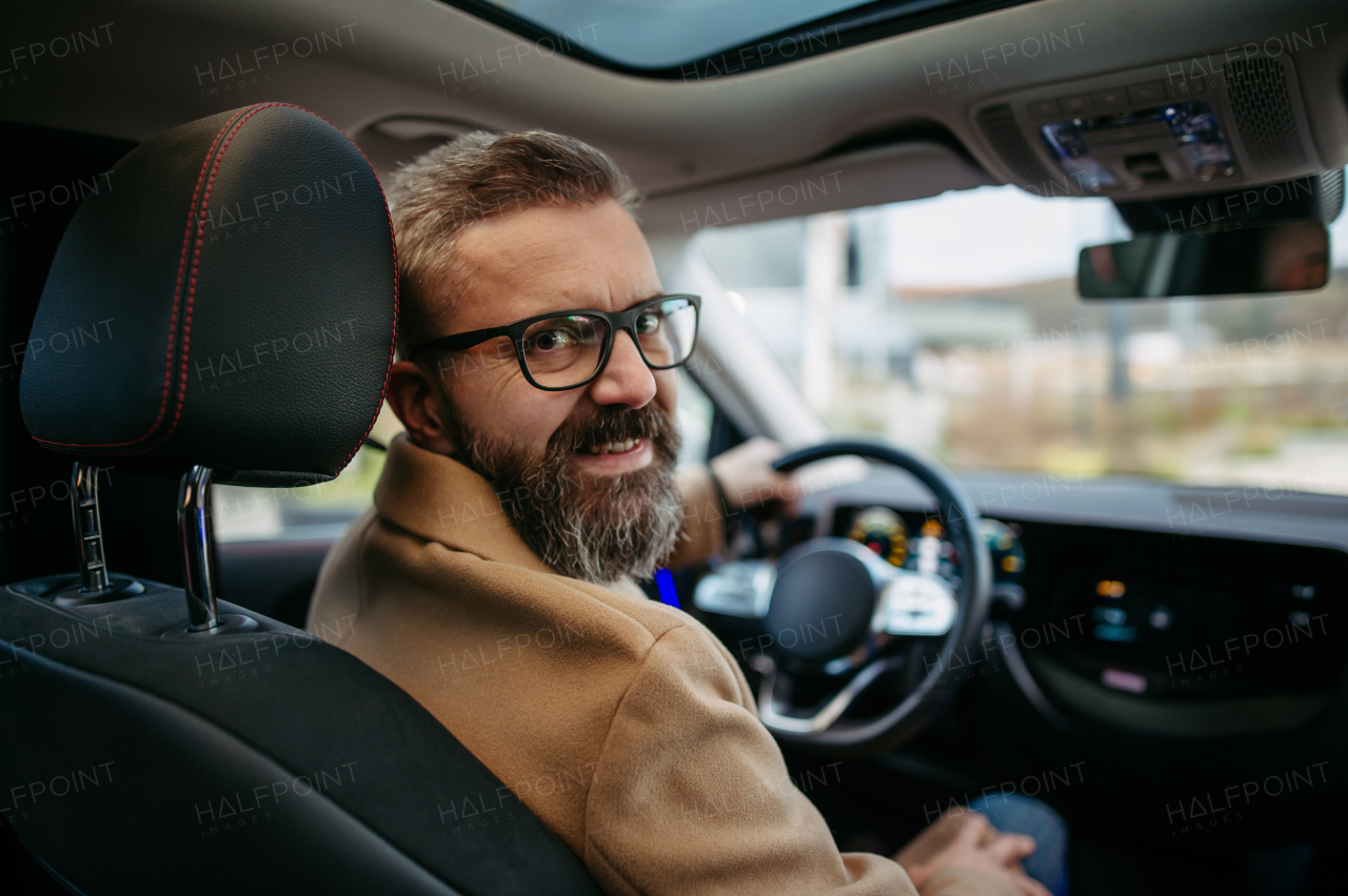 Portrait of mature handsome man sitting in electric car, looking back over the shoulder.