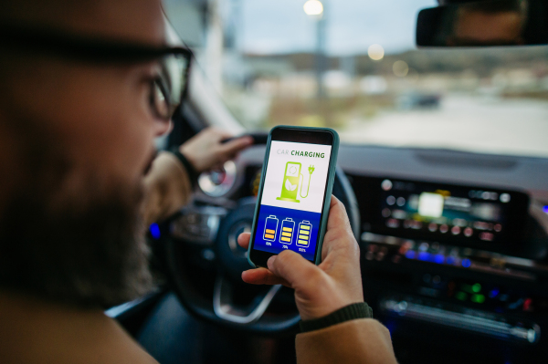 Close up of man using electric vehicle charging app, checking battery status, level on smart phone. Charging apps for monitoring electricity usage, locating charging stations.