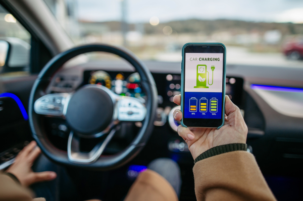 Close up of man using electric vehicle charging app, checking battery status, level on smart phone. Charging apps for monitoring electricity usage, locating charging stations.