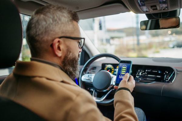 Close up of man using electric vehicle charging app, checking battery status, level on smart phone. Charging apps for monitoring electricity usage, locating charging stations.