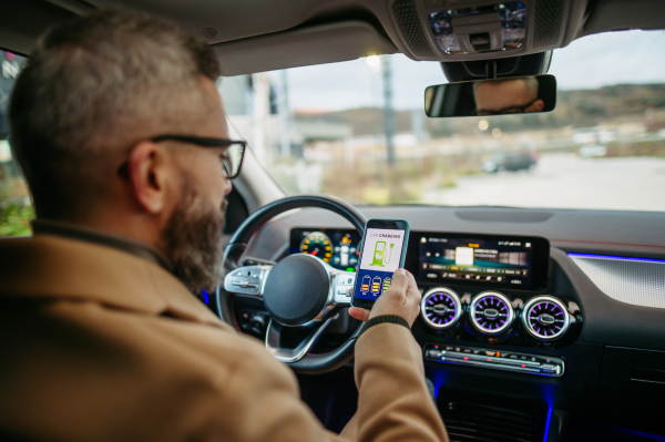 Close up of man using electric vehicle charging app, checking battery status, level on smart phone. Charging apps for monitoring electricity usage, locating charging stations.