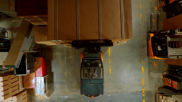 A top view of warehouse worker driving forklift. Warehouse worker preparing products for shipmennt, delivery, checking stock in warehouse.