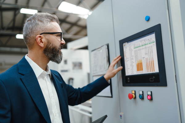 Production manager standing in modern industrial factory, controlling production process. . Manufacturing facility with robotics, robotic arms and automation.