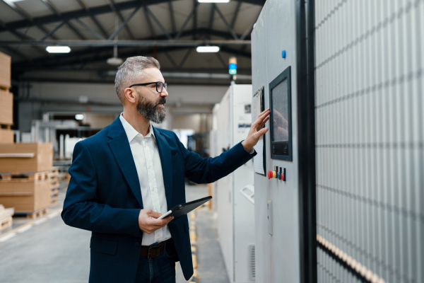 Production manager standing by control panel in modern industrial factory, controlling production process. . Manufacturing facility with robotics, robotic arms and automation.