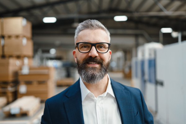 Portrait of project manager standing in modern industrial factory. Manufacturing facility with robotics, robotic arms and automation. Storing products and materials in warehouse.