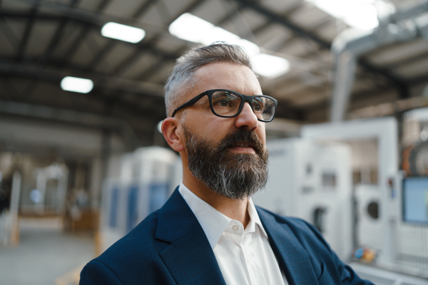 Portrait of engineer, project manager standing in modern industrial factory. Manufacturing facility with robotics, robotic arms and automation. Storing products and materials in warehouse.