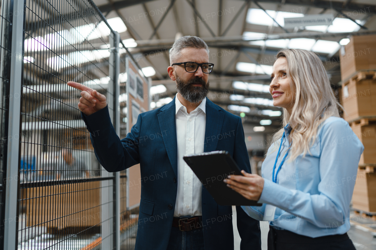 Female engineer and male production manager standing in modern industrial factory, talking about production. Manufacturing facility with robotics, robotic arms and automation.