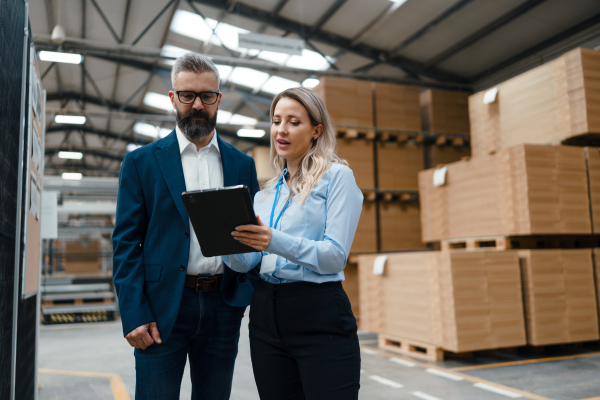 Female engineer and male production manager standing in modern industrial factory, talking about production. Manufacturing facility with robotics, robotic arms and automation.