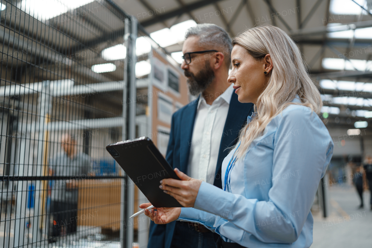 Female engineer and male production manager standing in modern industrial factory, talking about production. Manufacturing facility with robotics, robotic arms and automation.