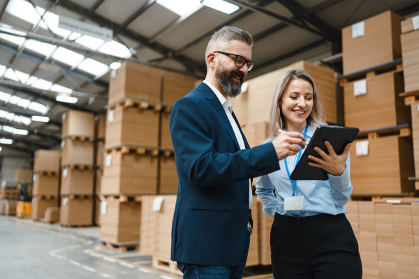 Female warehouse manager talking with logistics employee in warehouse, planning transport of products, goods, talking shipping process. Storing products and materials in warehouse.