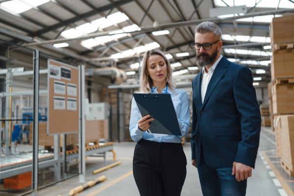 Female warehouse manager talking with logistics employee in warehouse, planning transport of products, goods, talking shipping process. Storing products and materials in warehouse.