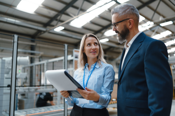 Female engineer and male production manager standing in modern industrial factory, talking about production. Manufacturing facility with robotics, robotic arms and automation.