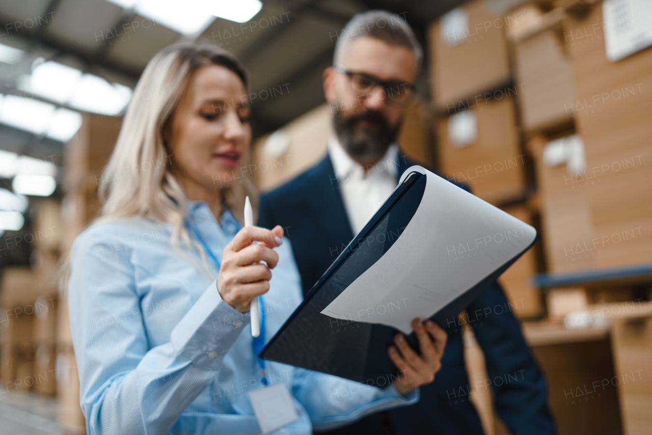 Female warehouse manager talking with logistics employee in warehouse, planning transport of products, goods, talking shipping process. Storing products and materials in warehouse.