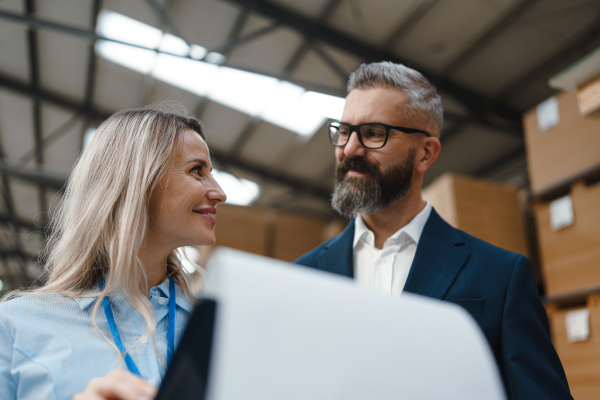 Female warehouse manager talking with logistics employee in warehouse, planning transport of products, goods, talking shipping process. Storing products and materials in warehouse.