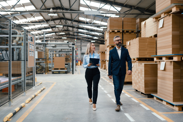 Female engineer and male project manager standing in modern industrial factory, talking about production. Manufacturing facility with robotics, robotic arms and automation.